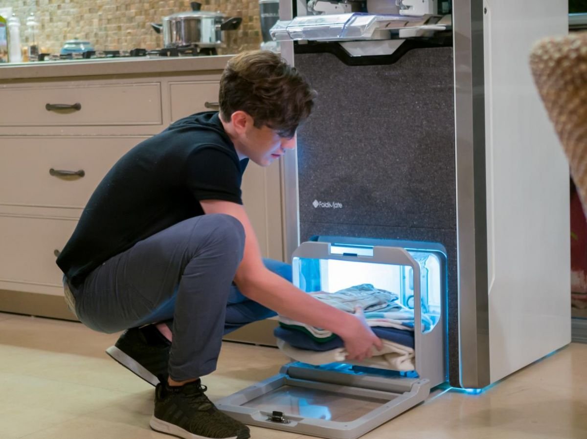 A young boy removes his impeccably folded and ironed clothes from the FoldiMate machine, offering fast, quality results. Find out how this innovative solution simplifies folding and ironing on ar.foldimateofficial.com.